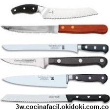 Afilador de cuchillos eléctrico. el cuerpo de plástico es gris-negro. se  inserta un cuchillo de cocina en el afilador. en primer plano hay cuchillos  y verduras picadas.